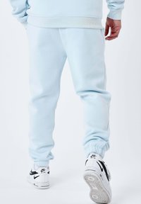 Lichtblauwe joggingbroek van zachte stof, met geribbelde boorden en zijnaden. Gecombineerd met witte sneakers met zwarte accenten.