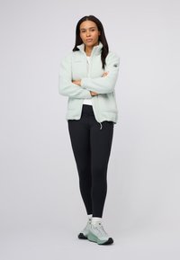 Jasno-miętowa polarowa kurtka z wysokim kołnierzem, w zestawie z czarnymi legginsami i miętowymi butami. Miękka faktura, lekka konstrukcja, casualowy styl.