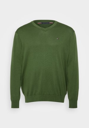 Grüner V-Ausschnitt Pullover aus glattem Strickmaterial. Mit langen Ärmeln und einem kleinen, markierten Logo auf der Brust. Lässiger Schnitt mit geripptem Saum.