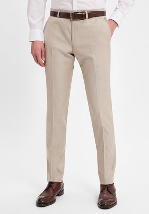 Helle beige Anzughose mit geradem Schnitt, die über eine glatte Textur und zwei seitliche Taschen verfügt, getragen mit einem braunen Ledergürtel und braunen Schuhen.