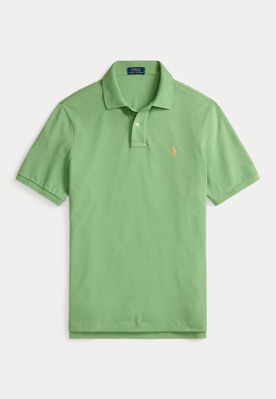 Camisa polo em verde pastel, com mangas curtas, em material de algodão. Apresenta uma pala com dois botões e um logótipo bordado em laranja.