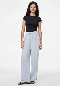 Črna prilegajoča majica in svetlo modre hlače širokega kroja z teksturiranim zaključkom. Hlače imajo pas z vrvico. Črne sandale dopolnjujejo obleko.