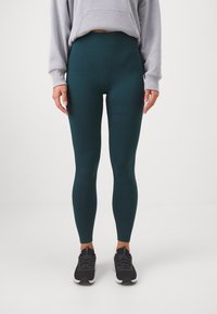 Mėlynos leggings su tamprių audiniu ir aukštu liemeniu. Lygi tekstūra su subtiliais vertikaliais raibuliavimo akcentais viršutiniame šlaunies plote.