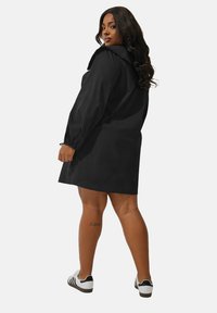 Svart klänning med puffärmar och volangkrage, över knä-längd, tillverkad av glatt tyg. Kombinerad med svart och vita sneakers.