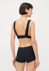 Czarny bikini top z prążkowanym wykończeniem, szerokimi ramiączkami i niskim tyłem, zestawiony z pasującymi, wysokimi szortami o teksturowanym wykończeniu.