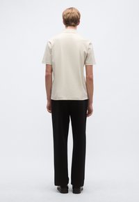 Svetlo béžové polokošeľa s krátkymi rukávmi, doplnená čiernymi nohavicami s rovnými nohavicami. Oblečenie má jednoduchý, čistý dizajn.