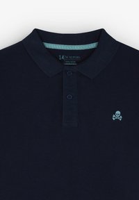 Polo azul marino de algodón con cuello, tapeta de dos botones y un pequeño logotipo de calavera azul claro en el pecho.