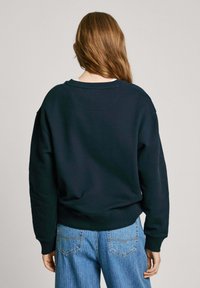 Mörkblå sweatshirt med rund halsringning och avslappnad passform, med ribbade manschetter och nederkant. Tillsammans med blå högmidjade jeans.