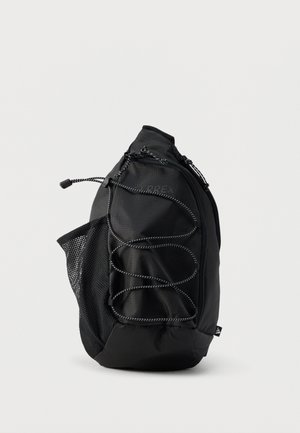 Černý batoh Terrex s elastickým předním lankem, boční síťovou kapsou a hlavním kapsou na zip, zobrazený na jednobarevném pozadí.