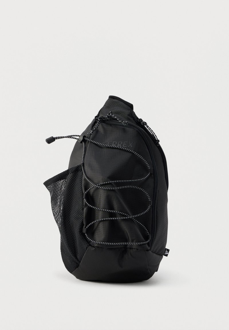 Μαύρο σακίδιο πλάτης Terrex με ελαστικό κορδόνι μπροστά, πλαϊνή τσέπη από δίχτυ και κύριο διαμέρισμα με φερμουάρ, εμφανισμένο σε απλό φόντο.