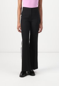 Pantaloni neri a palazzo con strisce laterali, vita alta e una texture liscia. Abbinati a un top rosa attillato e scarpe nere.