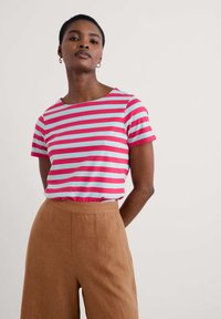 T-shirt rayé présentant des rayures alternées rose et bleu clair, avec un col rond et des manches courtes. Associé à un pantalon beige taille haute.