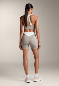 Világosszürke sportos öltözet, ujjatlan, magas hátú crop topból és hozzá illő, magas derekú sortból áll, sima tapintással és kontrasztos részletekkel.