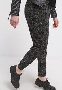 Czarne, strukturalne spodnie dresowe z subtelnym wzorem, posiadające elastyczny pasek w talii i zwężane mankiety, w zestawie z czarnymi, perforowanymi sneakersami.