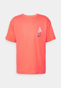 Coral cotton t-shirt with a round neck, short sleeves, featuring a colorful sail graphic and a black Nike logo on the chest.