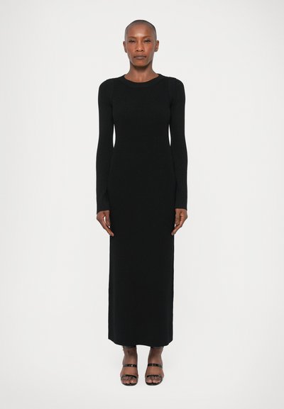 Robe en maille côtelée noire à manches longues, avec une silhouette ajustée, un col rond et une longueur jusqu'aux chevilles ; assortie de sandales noires à lanières.