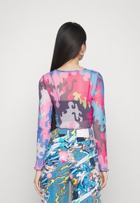 Langärmlige, durchsichtige Bluse mit bunten, gewellten Mustern in Pink, Blau und Grau, kombiniert mit gemusterten, hoch taillierten Hosen in lebhaften Farben.