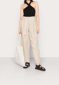 Top nero a coste con collo all'americana, pantaloni a vita alta in lino beige con cintura, borsa a righe e sandali platform neri.