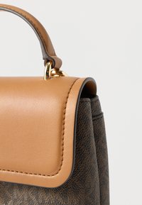 Borsa marrone dalla texture morbida con patta e manico in pelle color cuoio, con dettagli in metallo dorato e cuciture lungo i bordi.