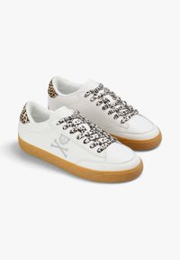 Zapatillas de cuero blancas con cordones de print de leopardo y acentos traseros, logotipo de calavera gris en el lateral y una suela de goma marrón.