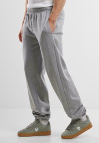 Pantalons de survêtement gris avec une taille élastique, deux poches latérales et des poignets resserrés. Associés à des baskets vertes avec un logo blanc.