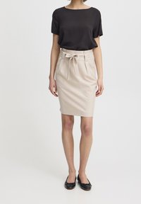 Svart kortärmad blus i kombination med en beige knälång midikjol, med ett knytbälte och sidofickor, kompletterad med svarta ballerinas.