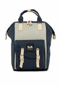 Sac à dos en toile bleu marine et gris avec des accents beige, deux poignées supérieures, une poche à rabat sur le devant avec des sangles, et une fermeture éclair.