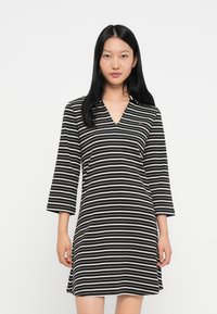 Sukienka w paski z czarno-białym wzorem, dekoltem w serek oraz rękawami o długości 3/4. Wykonana z lekkiego materiału, o luźnym kroju.