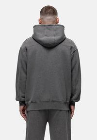 Sweatshirt à capuche gris avec une coupe décontractée, doté d'un tissu texturé, de larges manches et de poignets côtelés, conçu pour le confort et les tenues décontractées.