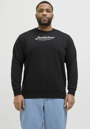 Schwarzer Sweatshirt mit rundem Halsausschnitt und langen Ärmeln, mit weißem LOGO-Text auf der Brust. Kombiniert mit hellblauen Jeans.