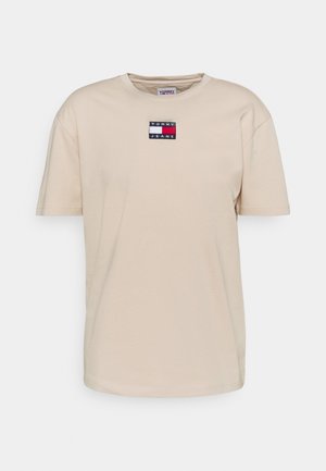 Beiges Baumwoll-T-Shirt mit kurzen Ärmeln und Rundhalsausschnitt. Auf der Brust befindet sich ein kleines, rechteckiges Logo-Patch in Marineblau, Rot und Weiß.