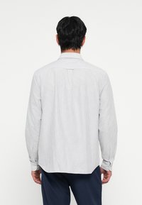 Striped long-sleeve shirt in white and light blue cotton, featuring a standard collar, button cuffs, and a yoke detail at the back.