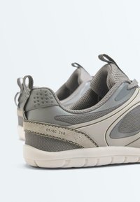 Paire de baskets de sport grises avec des détails en mesh et en suède, semelles rembourrées et languettes au talon sur fond blanc.