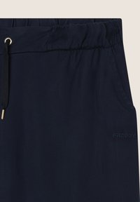 Pantalon en tissu élastique navy avec cordon de serrage et quincaillerie dorée. Présente un logo tonal subtil. Texture lisse, design décontracté et sans poches visibles.