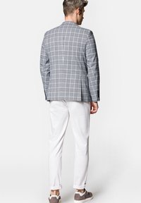 Szary w kratę blezer o dopasowanym kroju, w parze z białymi wąskimi spodniami i szarymi butami, z tkaniną o fakturze i klapami w szpic.