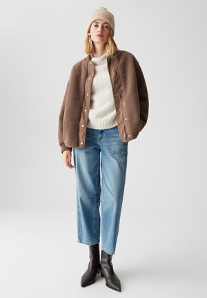 Brown fleece jacket with a smooth brown front, white knit sweater, light blue relaxed-fit jeans, and black pointed ankle boots.