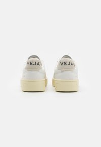 Sneakers in white leather with beige accents. Features rounded back, soft texture, and embossed logo on heel. Light, durable rubber sole.