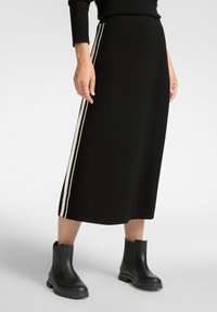 Zwarte midi-rok met aan elke kant twee verticale witte strepen, gemaakt van een gladde stof. Gecombineerd met zwarte enkellaarsjes.