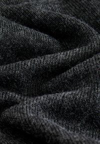 Schwarzer, strukturierter Stoff mit einer weichen, gestrickten Optik, der sichtbare Fasern und einen sanften Fall aufweist und so eine subtile Tiefe und Dimension erzeugt.