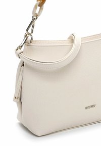 Bolso de cuero beige con textura suave, asa redonda y cierre en tono dorado. Presenta un logo en relieve y detalles sutiles de costura.