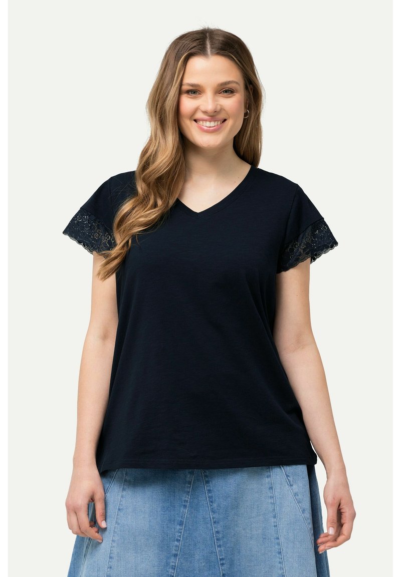 Camiseta de cuello en V de color marino con ribete de encaje en las mangas cortas. Tejido suave, corte relajado y un diseño ligero apto para uso casual.