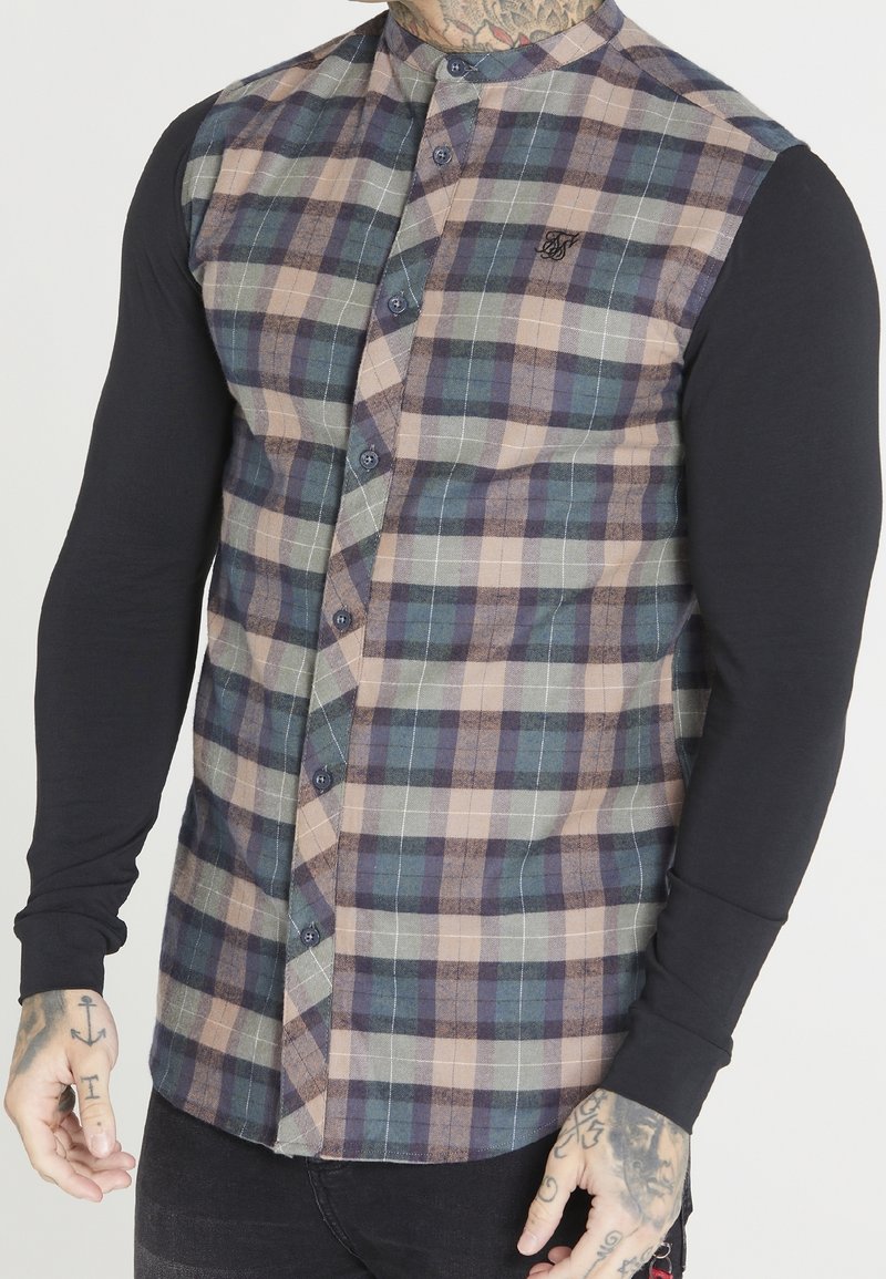 Camisa de manga larga con un frente de cuadros abotonado en verde, azul y beige, con mangas negras y un logo bordado en el pecho izquierdo.