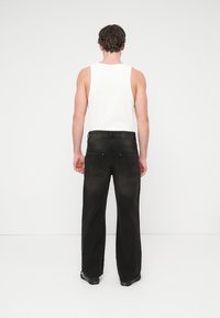 Μαύρο τζιν παντελόνι φαρδιάς γραμμής με υφή στην πίσω πλευρά, δύο πίσω τσέπες και λείο ζωνάρι, συνδυασμένο με λευκό αμάνικο τοπ.