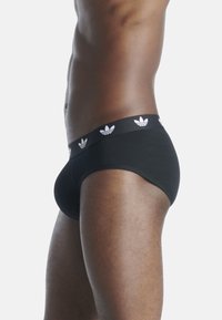 Zwarte sportieve onderbroeken van gladde stof met een aansluitende snit. Voorzien van een zwarte tailleband versierd met witte Adidas-logo's.