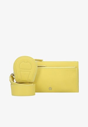 Billetera de cuero amarilla con correa ajustable, que presenta un acabado texturizado, un acento de logo plateado y un monedero redondo adjunto.