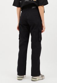 Schwarze Cargo-Hosen aus robustem Baumwollgemisch, mit Seitentaschen, hoher Taille und lockerer Passform, versehen mit sichtbaren Nähdetails.