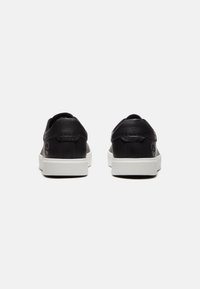 Zwarte leren sneakers met een witte rubberen zool. Soepele textuur met een minimaal ontwerp en logo detail aan de zijkant.