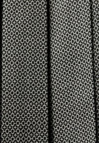 Tissu tissé noir et blanc avec un petit motif géométrique répétitif formant des croix et des points entrelacés.