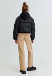 Černá péřová bunda, zkrácený design, s širokými rukávy, v kombinaci s béžovými cargo kalhotami. Černé platformové boty s robustními podrážkami.