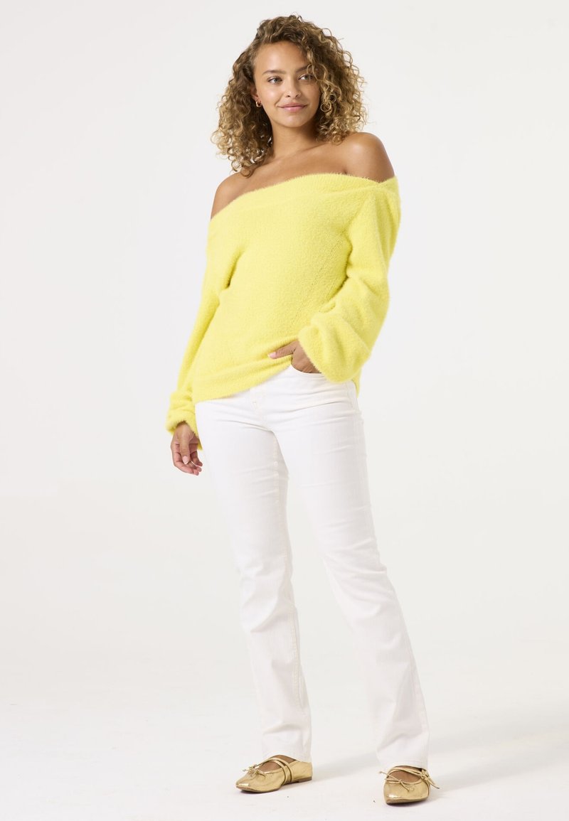 Pull jaune à épaules dénudées en tissu doux et texturé, associé à un jean blanc ajusté et des ballerines dorées. Ensemble simple et décontracté.